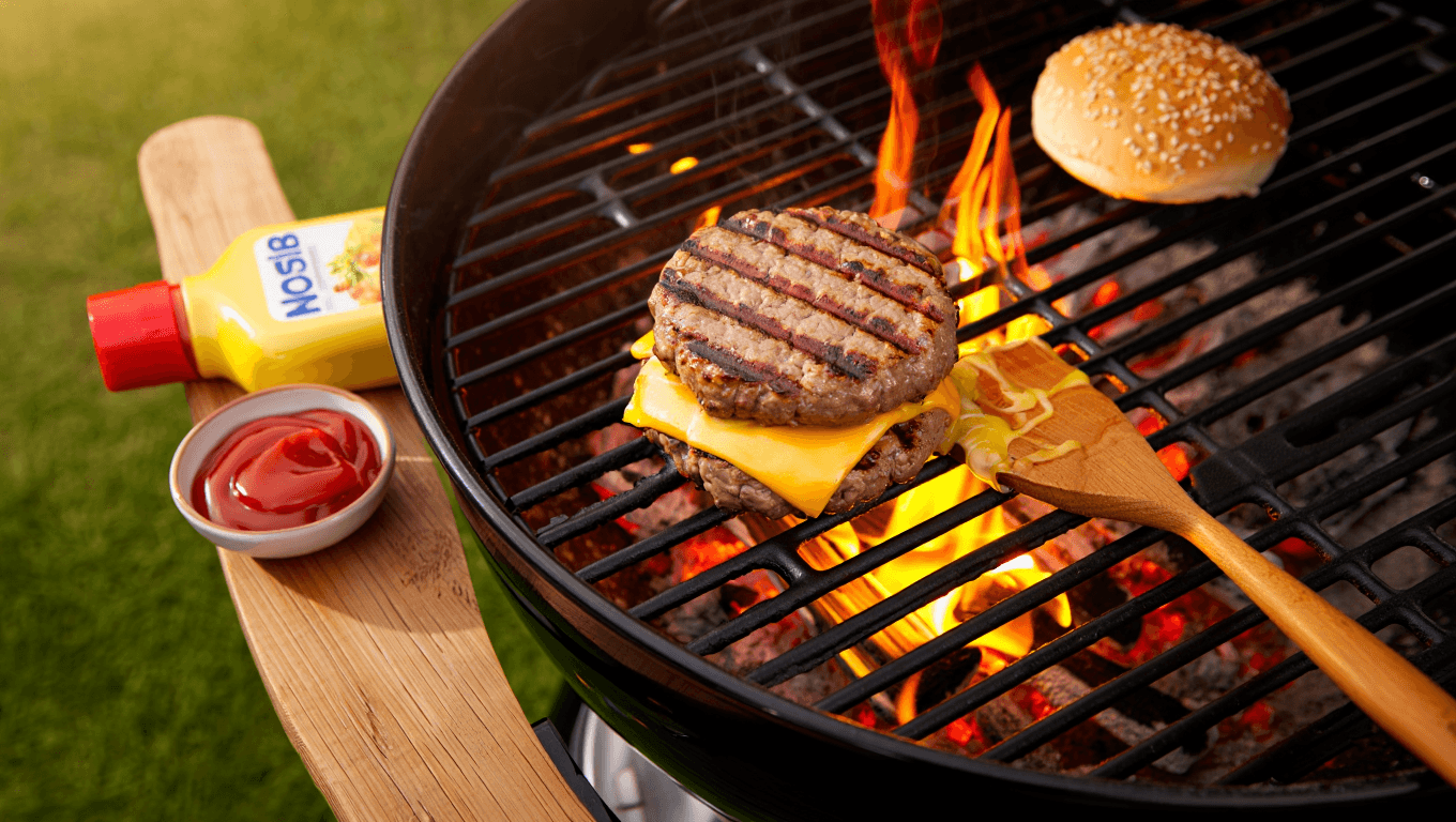 Cheeseburger with toppings on a while plate with chips in the background