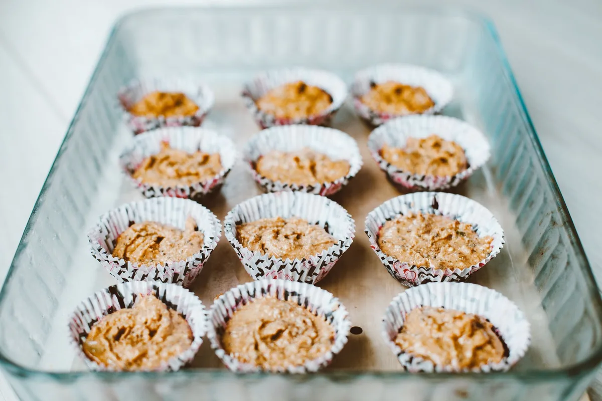 Batter being spooned into a lined mini muffin pan, three-quarters full, ready for the oven