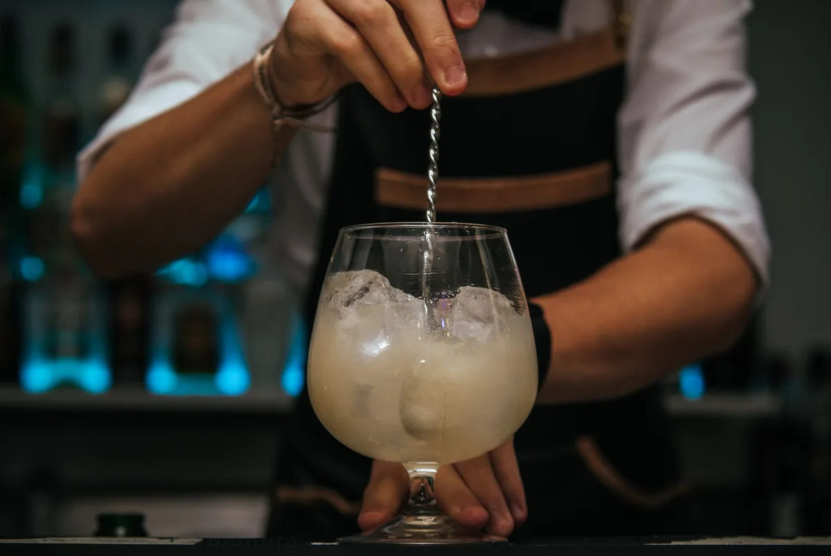 Bartender stirring cocktail ingredients with ice in a mixing glass