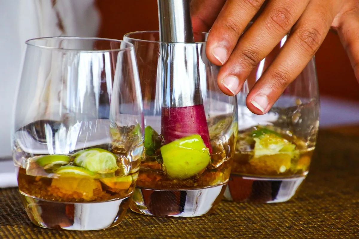 Bartender gently muddling fresh lime wedges and sugar in a glass