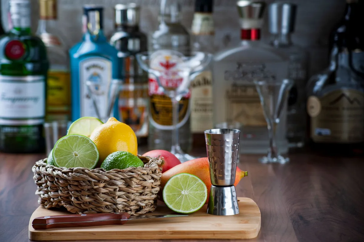Tropical rum cocktail ingredients arranged on bar: rum bottles, fresh lime, mango syrup and Sauvignon Blanc