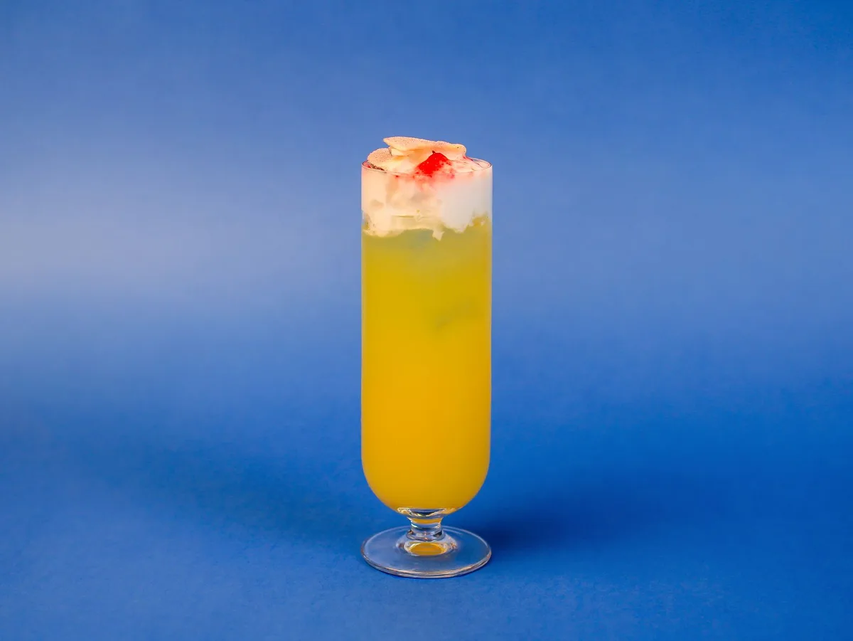 Tropical rum cocktail being prepared with fresh citrus and mango garnish in a coupe glass
