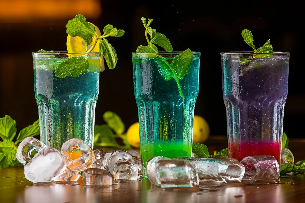 Copa Collins alta llena de hielo con cóctel de color ámbar, adornada con hojas de menta, ruedas de limón y fresas