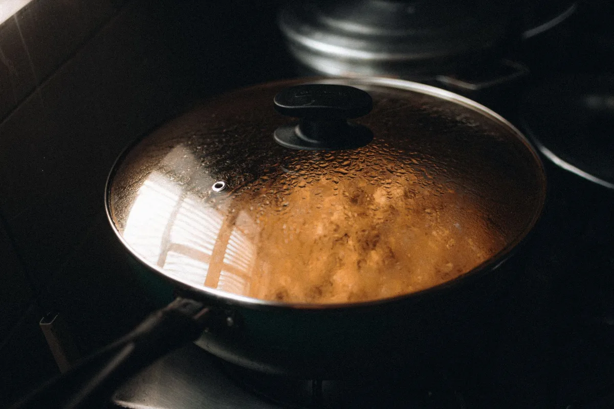 A pot of rice simmering on the stovetop with steam rising from the lid