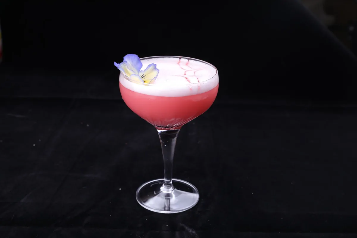 A chilled coupe glass with a creamy foam-topped amber cocktail and fresh nutmeg garnish
