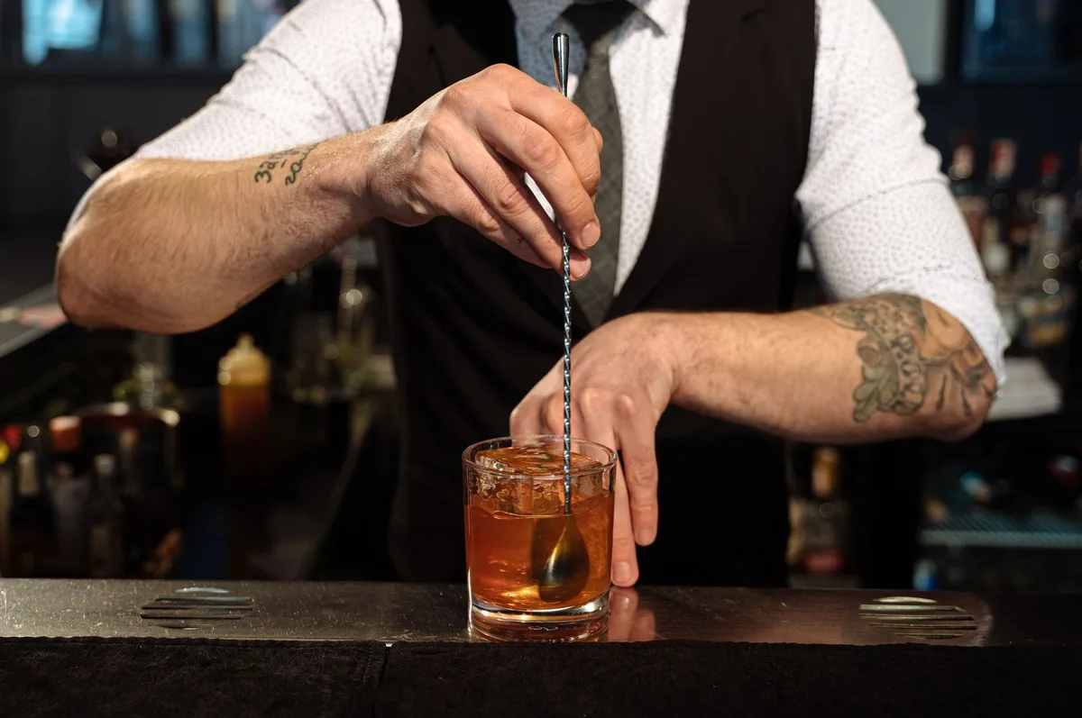 A bartender stirring a cocktail in a mixing glass with ice using a bar spoon