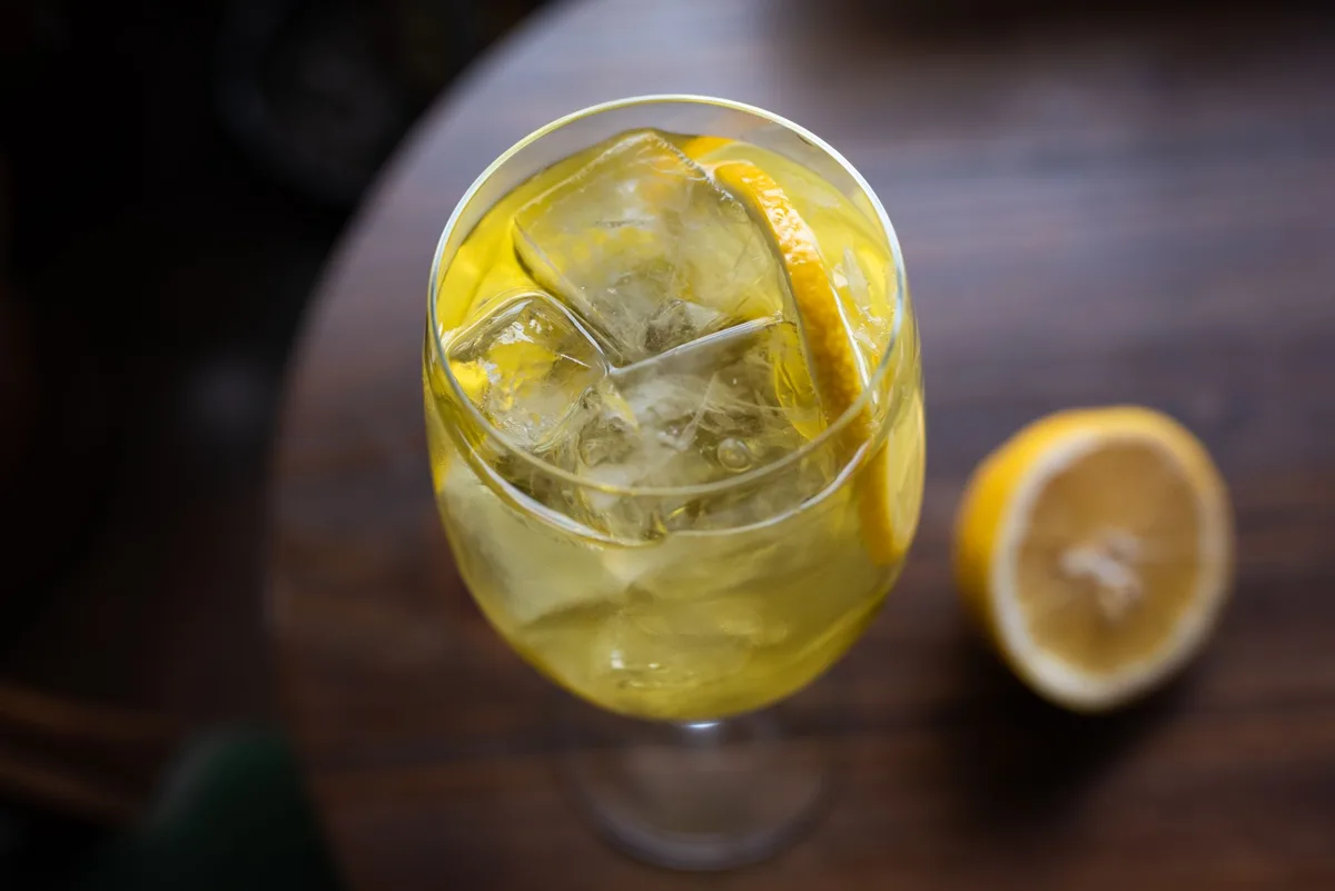 Verre contenant un cocktail au limoncello jaune vif avec glaçons et zeste de citron vert en garniture