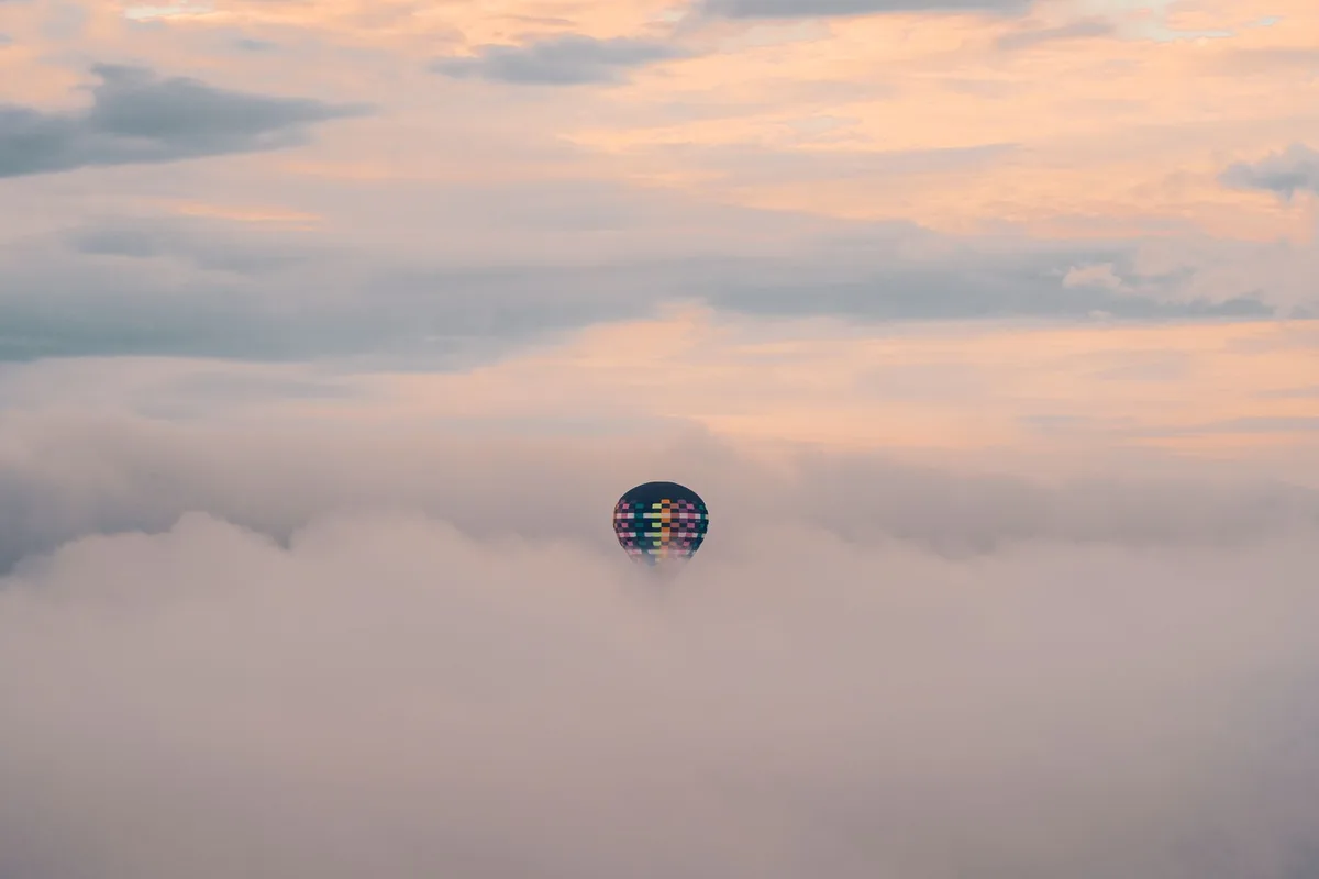 Vintage hot air balloon floating through dramatic storm clouds above landscape