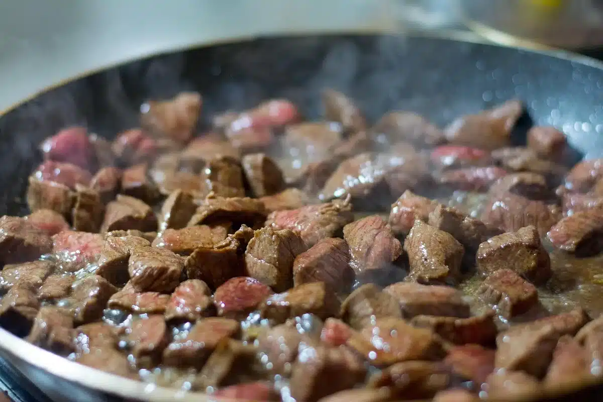 Patties being seared in a hot skillet with a spatula