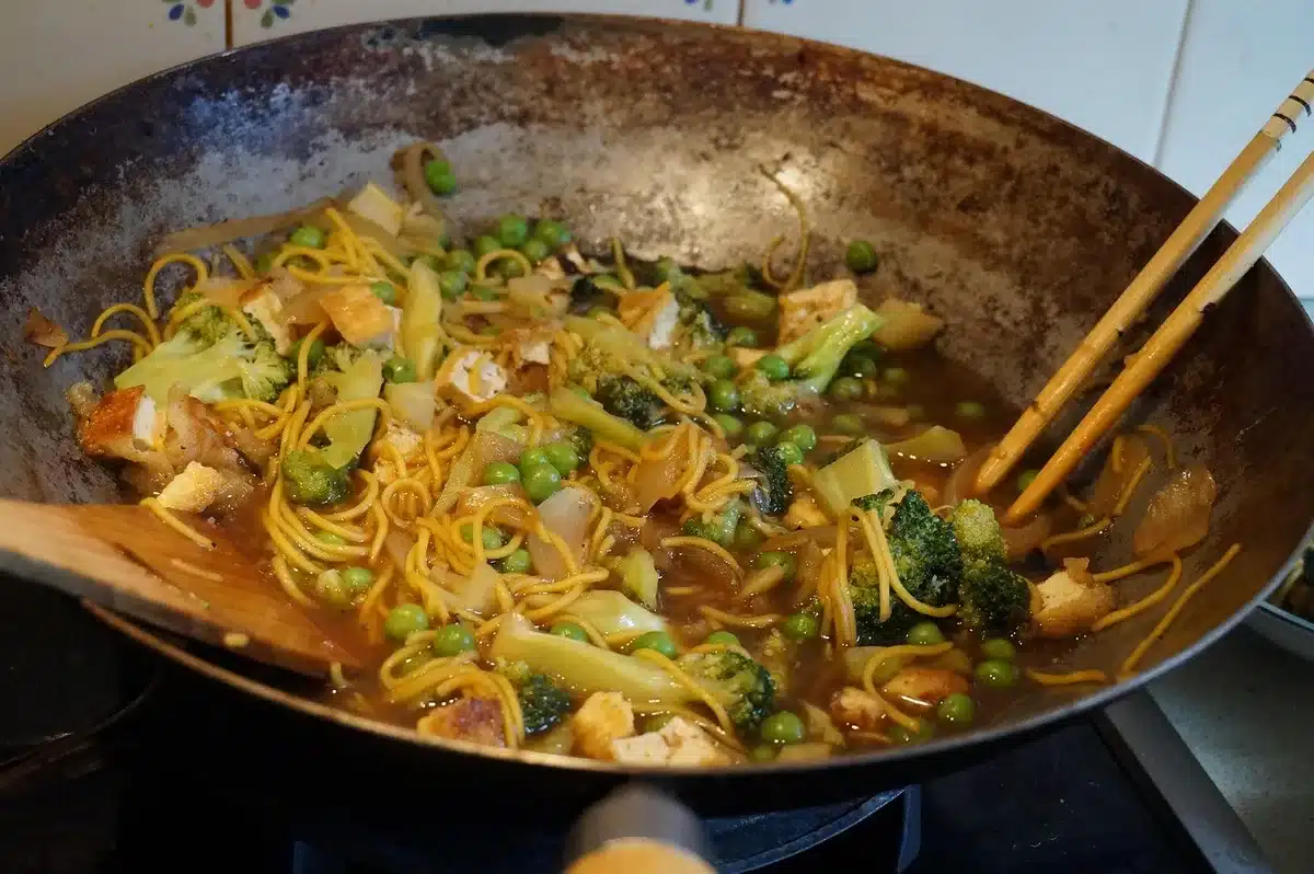 Wok avec nouilles sautées et spatule en bois sur feu vif