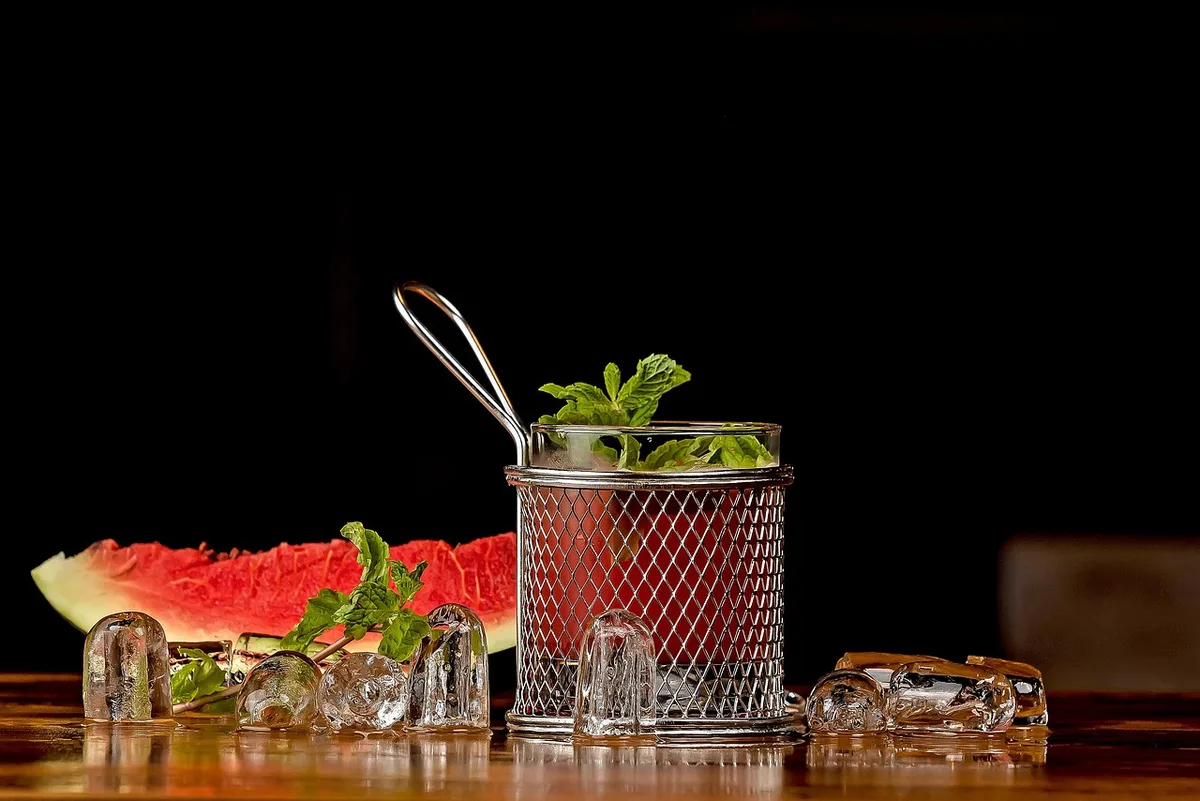 Shaker being double-strained into a rocks glass over ice in daylight