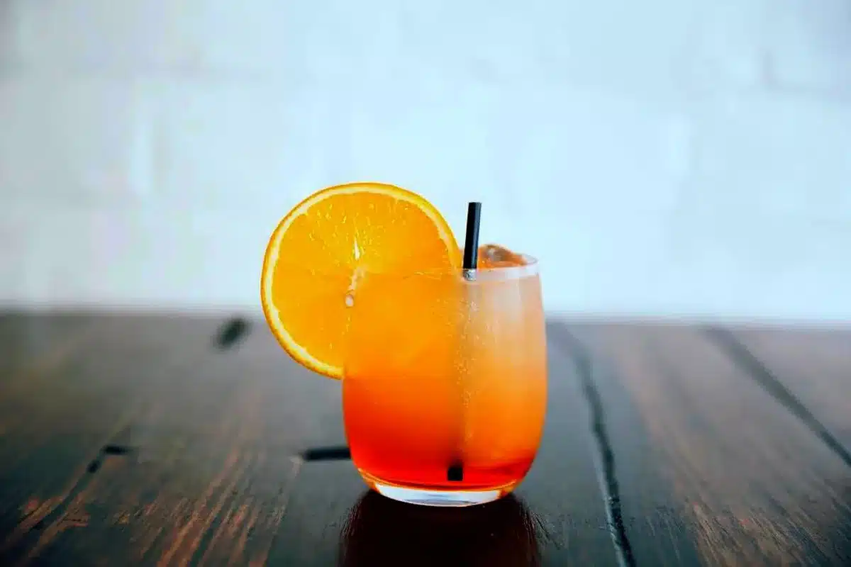Pale amber cocktail in a coupe with an orange twist garnish