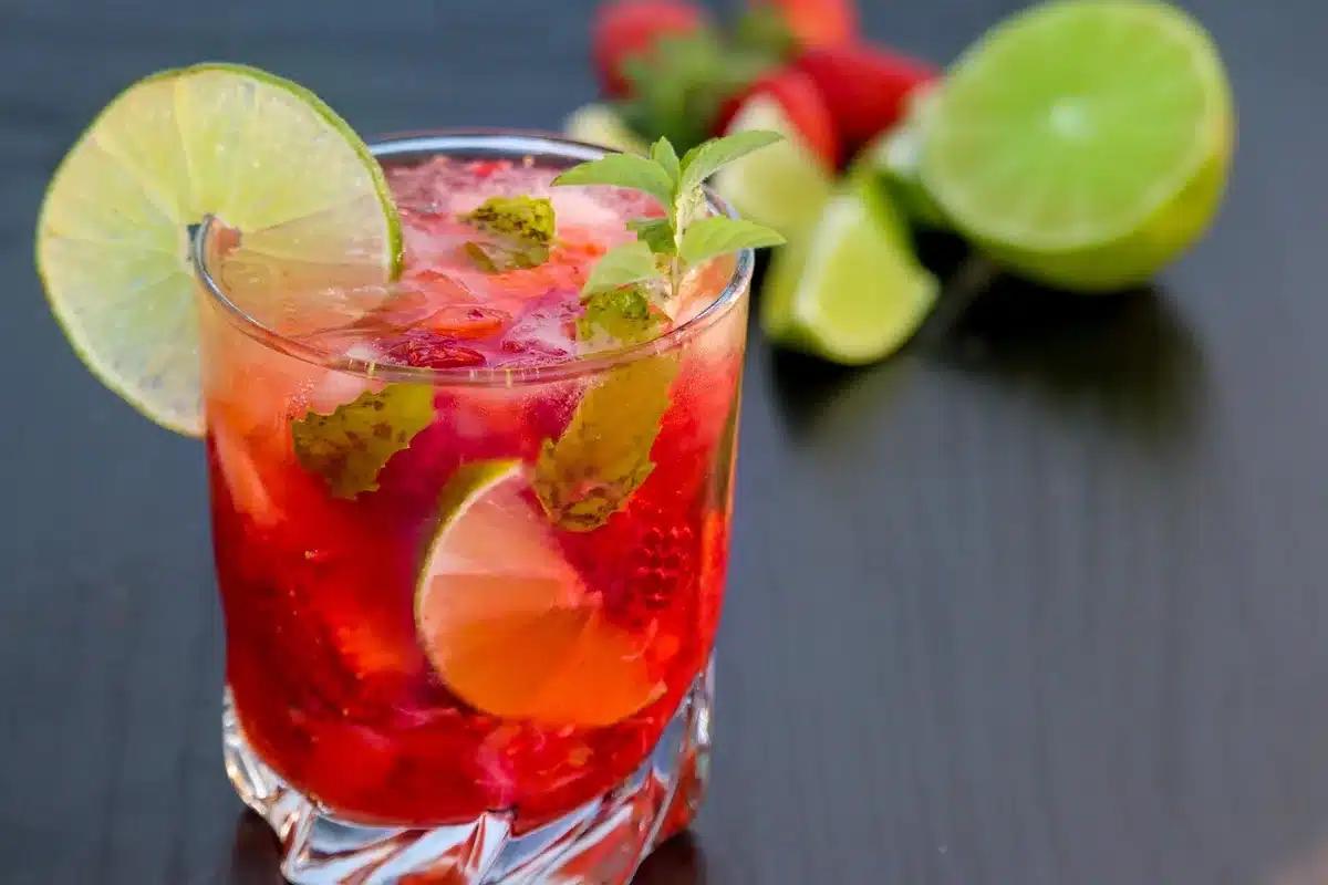 Chilled coupe with a pale gin margarita and sunken blackcurrants, lime wheel on rim